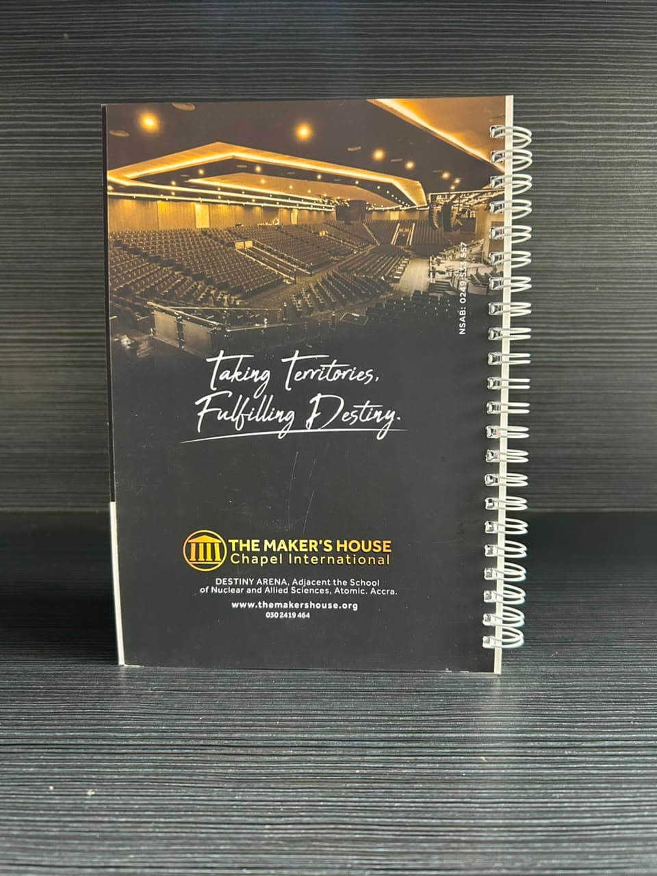 Back of the same notebook: a photograph of a large lit auditorium above a hand-lettered tagline and the church's gold logo.
